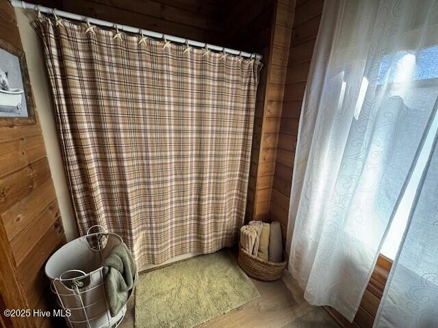 full bathroom with wooden walls, wood finished floors, and a shower with curtain