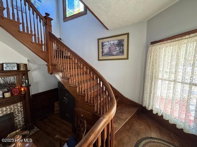 staircase featuring a stone fireplace, a textured ceiling, and wood finished floors