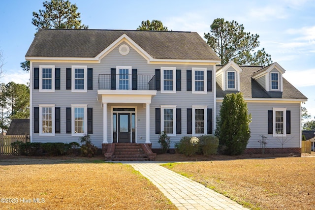 colonial house featuring a shingled roof, a front yard, crawl space, and a balcony