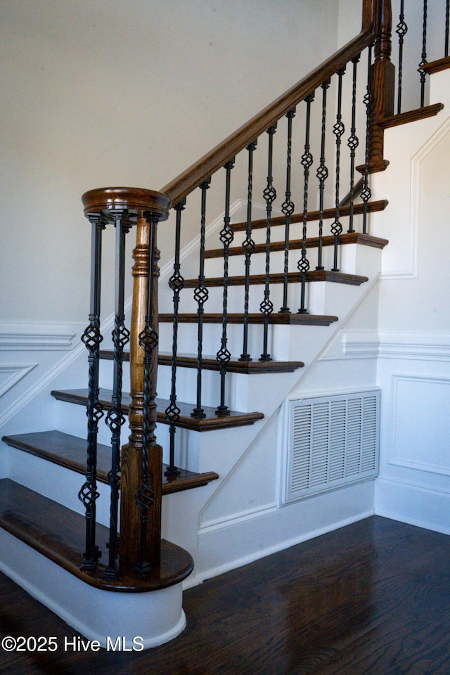 stairway featuring a wainscoted wall, wood finished floors, visible vents, and a decorative wall