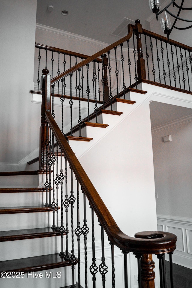 staircase with a notable chandelier, a wainscoted wall, a decorative wall, visible vents, and crown molding