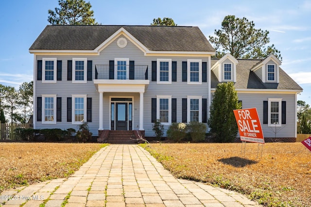 colonial inspired home featuring a balcony and a shingled roof