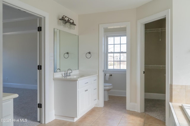 bathroom featuring a walk in closet, vanity, toilet, and tile patterned floors