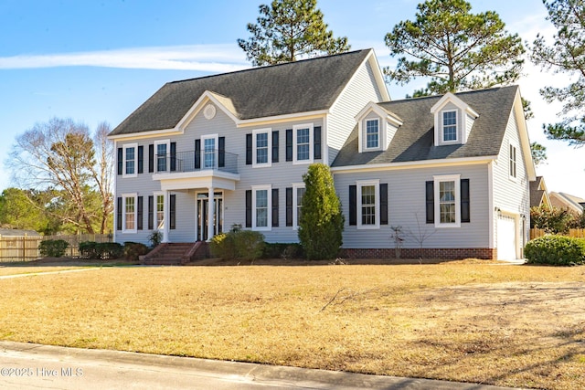 colonial-style house featuring roof with shingles, a front yard, fence, a balcony, and a garage