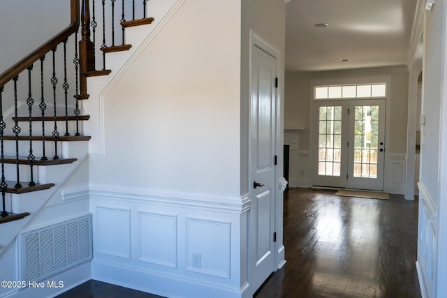 interior space featuring a decorative wall, a wainscoted wall, dark wood-type flooring, visible vents, and stairs