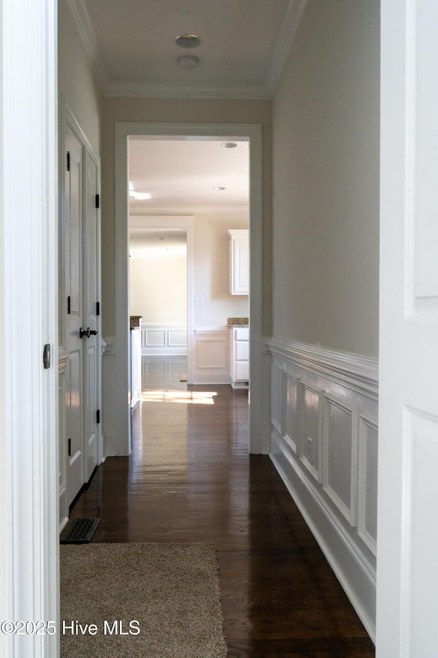 corridor featuring wainscoting, crown molding, and a decorative wall