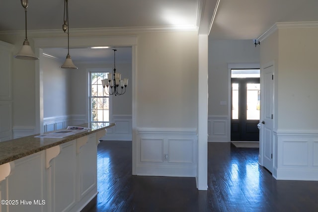 kitchen with hanging light fixtures, stone counters, wainscoting, and dark wood finished floors