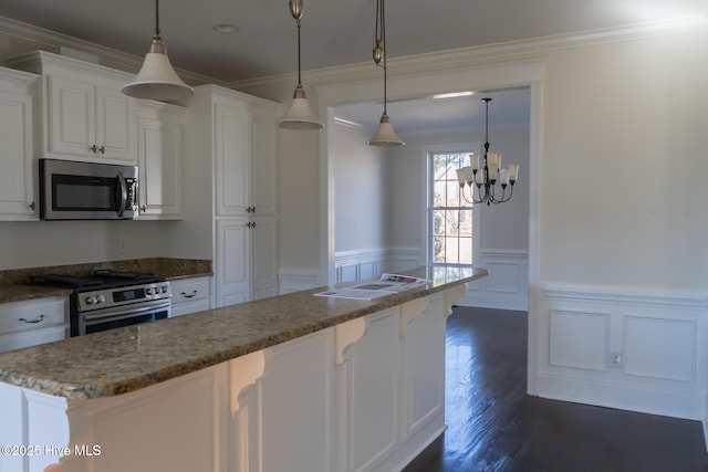 kitchen featuring white cabinets, dark wood finished floors, appliances with stainless steel finishes, ornamental molding, and dark stone countertops