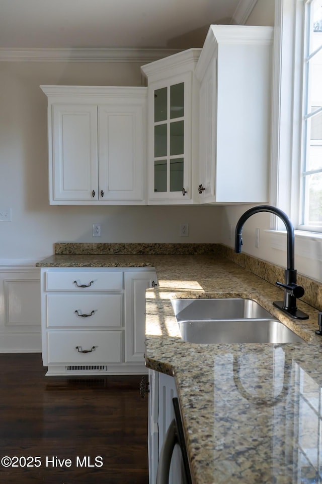 kitchen with glass insert cabinets, ornamental molding, light stone countertops, white cabinetry, and a sink