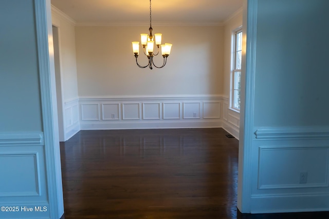 spare room with dark wood-type flooring, ornamental molding, and an inviting chandelier