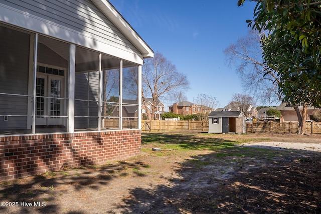 view of yard with a sunroom, a fenced backyard, an outdoor structure, and a storage shed