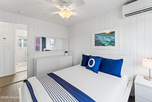 bedroom with electric panel, a ceiling fan, an AC wall unit, and wood finished floors