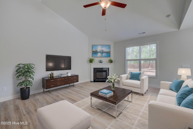 living area featuring light wood finished floors, baseboards, visible vents, and a glass covered fireplace