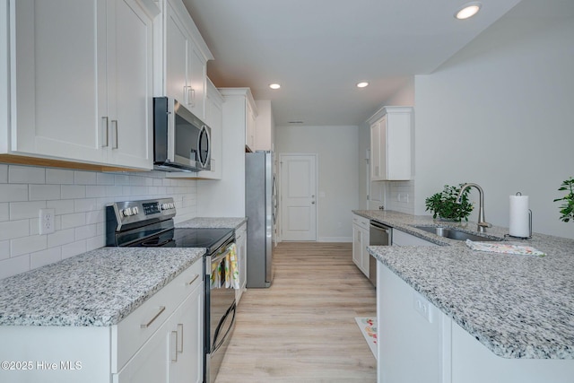 kitchen with white cabinets, appliances with stainless steel finishes, a sink, light wood-style floors, and backsplash