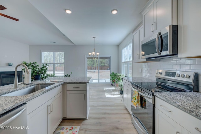 kitchen featuring decorative backsplash, a glass covered fireplace, light wood-style flooring, stainless steel appliances, and a sink