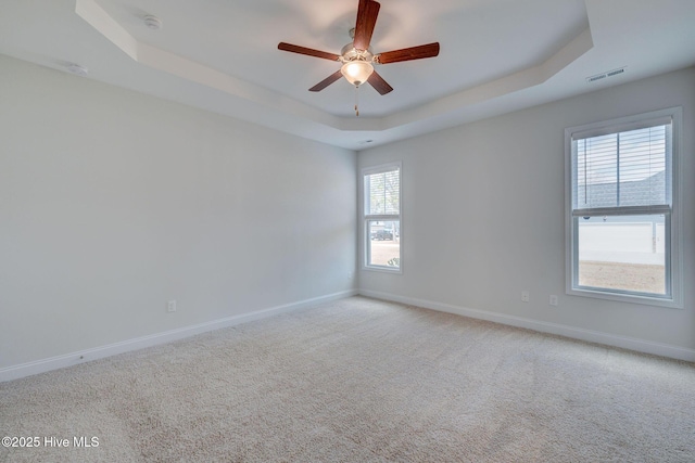 empty room with a tray ceiling, visible vents, light carpet, and baseboards