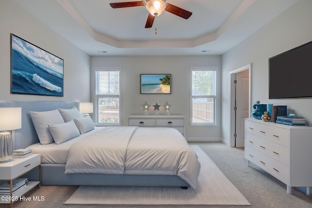 bedroom featuring visible vents, multiple windows, a tray ceiling, and light colored carpet