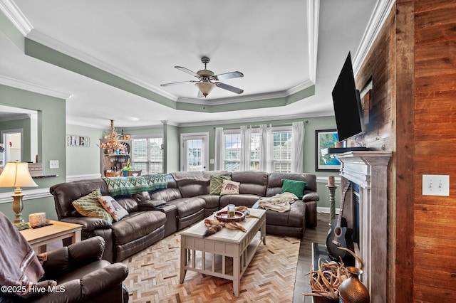 living room with ornamental molding, a tray ceiling, a fireplace, and ceiling fan