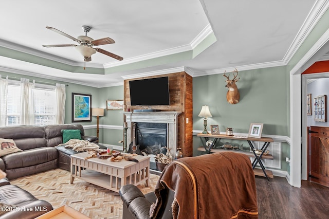 living area with a raised ceiling, a ceiling fan, a glass covered fireplace, wood finished floors, and crown molding