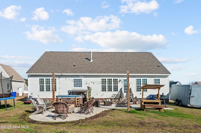 back of property featuring an outdoor fire pit, a lawn, a patio, roof with shingles, and a trampoline