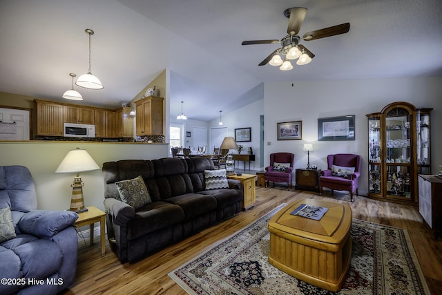 living area with a ceiling fan, vaulted ceiling, and wood finished floors