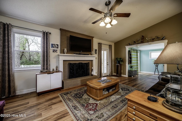 living area featuring baseboards, a brick fireplace, wood finished floors, and vaulted ceiling