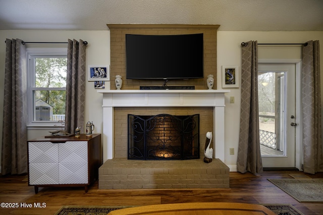 living room with a brick fireplace, a textured ceiling, and wood finished floors