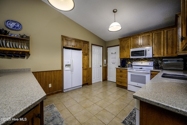 kitchen with white appliances, light tile patterned flooring, wainscoting, vaulted ceiling, and hanging light fixtures