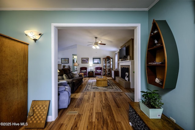 living area featuring a fireplace with raised hearth, built in shelves, ceiling fan, lofted ceiling, and wood finished floors