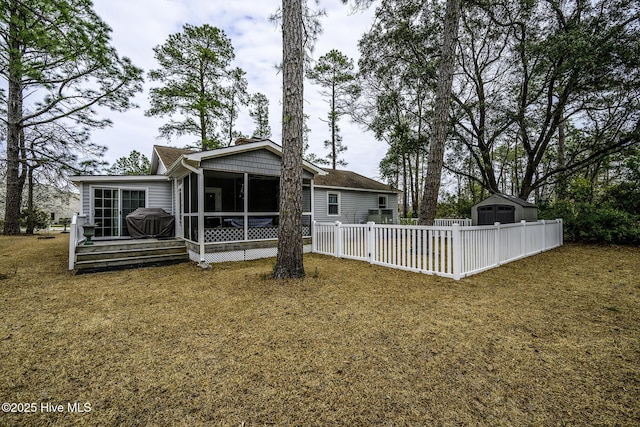 rear view of house featuring fence, a sunroom, an outdoor structure, a storage unit, and a lawn