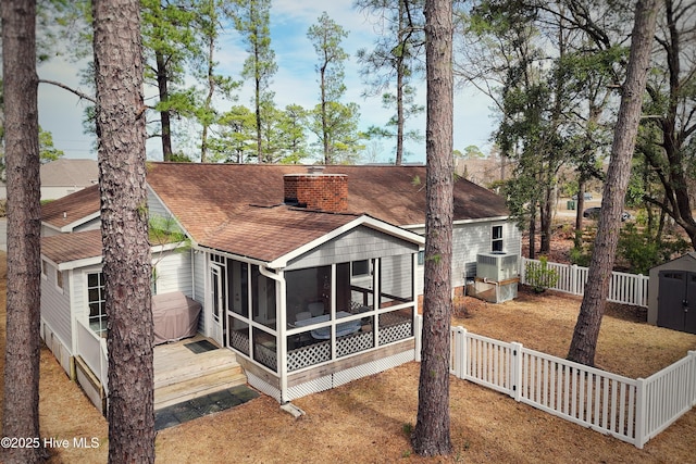 back of property featuring fence, roof with shingles, a sunroom, a chimney, and a storage unit