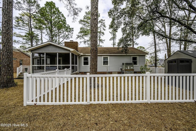 rear view of house with fence, a sunroom, a chimney, an outdoor structure, and a storage shed