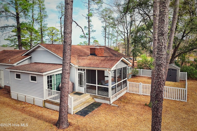 back of property featuring fence, a shed, a sunroom, a shingled roof, and an outdoor structure