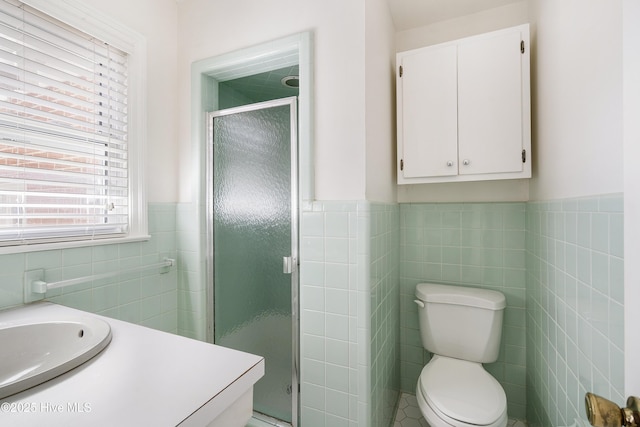 bathroom with tile walls, toilet, wainscoting, a sink, and a shower stall