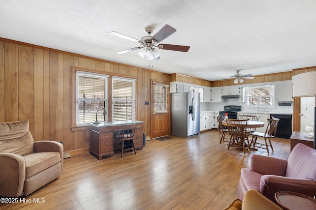 living room with a wealth of natural light, ceiling fan, wooden walls, and wood finished floors