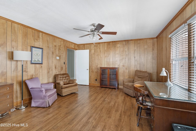 living area with ceiling fan, wooden walls, wood finished floors, and crown molding