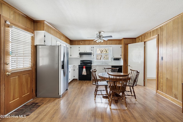 dining space featuring light wood-type flooring, ceiling fan, wooden walls, and a textured ceiling