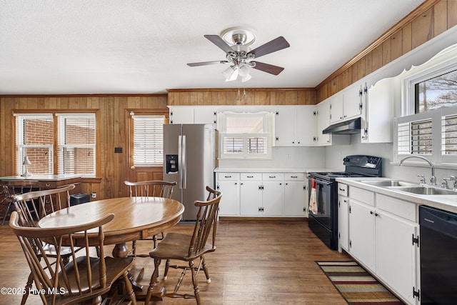 kitchen with dark wood finished floors, light countertops, a sink, under cabinet range hood, and black appliances