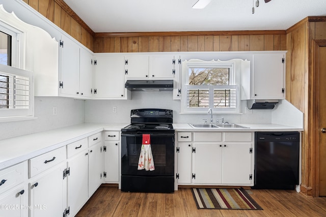 kitchen with under cabinet range hood, wood finished floors, a sink, white cabinets, and black appliances