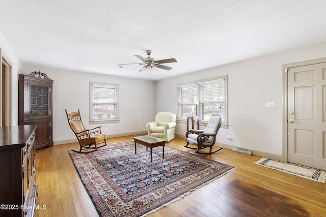 living area with a textured ceiling, a healthy amount of sunlight, baseboards, and light wood-style floors