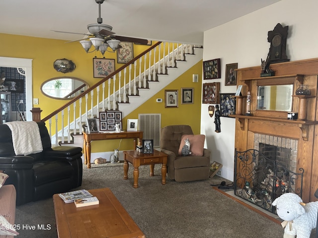 carpeted living room with a brick fireplace, visible vents, stairway, and a ceiling fan