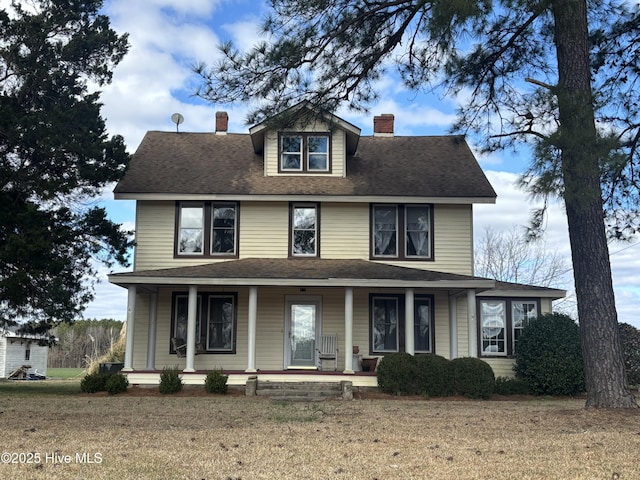 view of front of house with a front yard, covered porch, a chimney, and roof with shingles