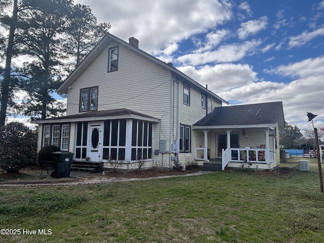 back of house featuring a lawn, a sunroom, a chimney, covered porch, and central AC