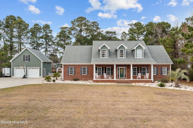 cape cod house with brick siding, a front lawn, concrete driveway, covered porch, and an outbuilding