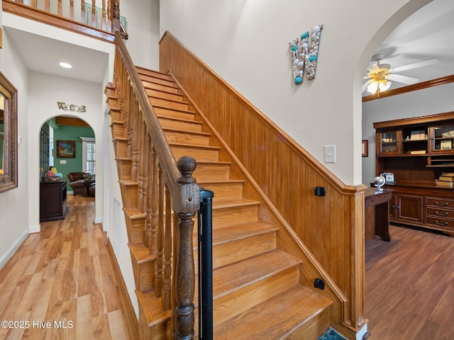 stairs with arched walkways, crown molding, a ceiling fan, and wood finished floors