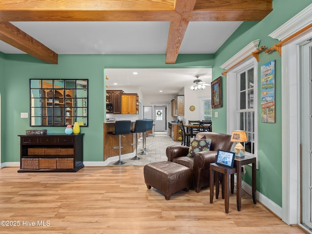 living room with ceiling fan, beamed ceiling, baseboards, and light wood-style flooring