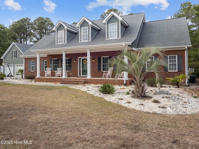 cape cod-style house featuring brick siding, a shingled roof, a front lawn, central air condition unit, and a porch