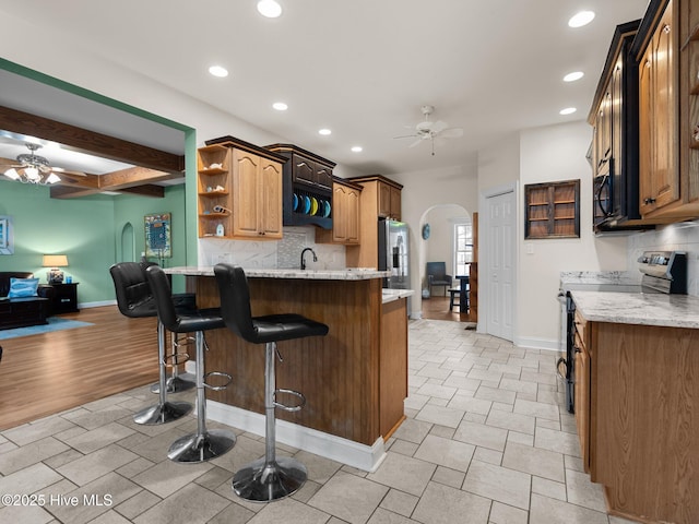 kitchen featuring arched walkways, stainless steel appliances, ceiling fan, and open shelves