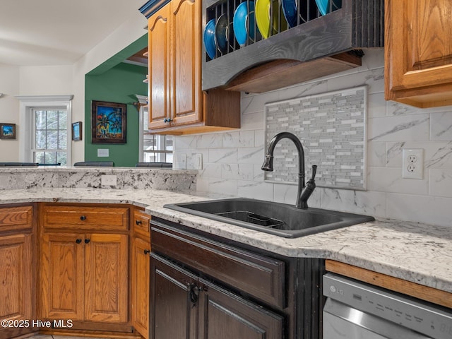 kitchen featuring tasteful backsplash, dishwasher, light stone countertops, and a sink