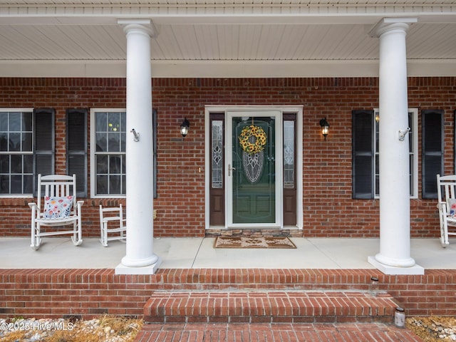 view of exterior entry featuring a porch and brick siding